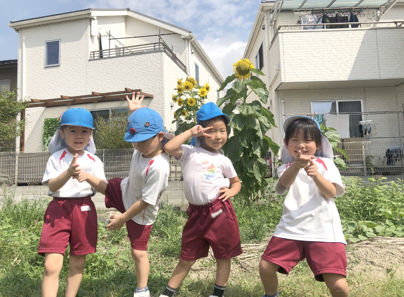 ひまわりの前でポーズをとる子どもたちの写真