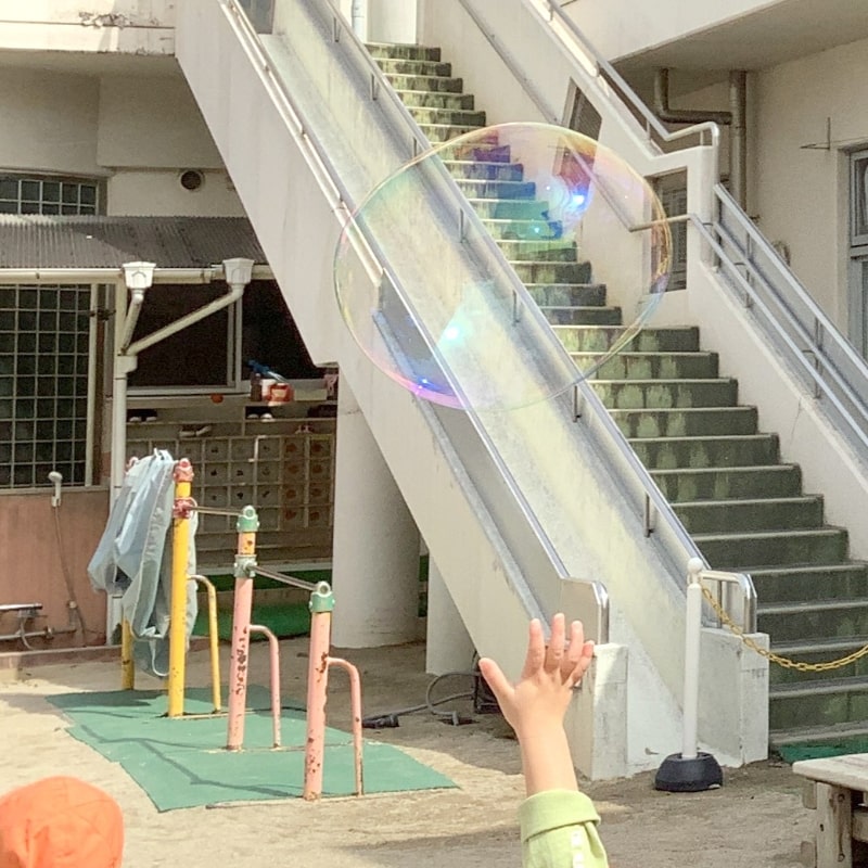 シャボン玉に手を伸ばす子どもの写真